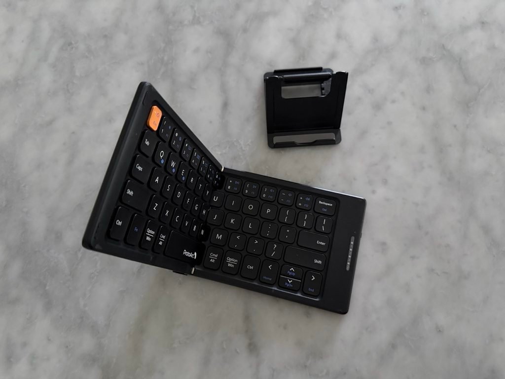 A half folded keyboard with a single orange key and a mobile phone stand.