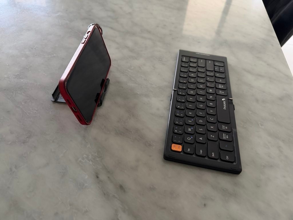 A wireless keyboard and an iPhone on a mobile stand.