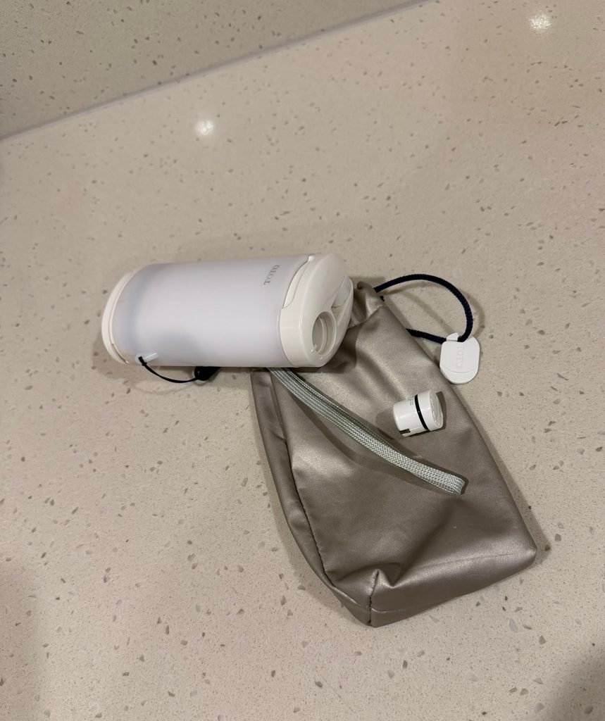A handheld TOTO travel bidet next to a grey pouch.