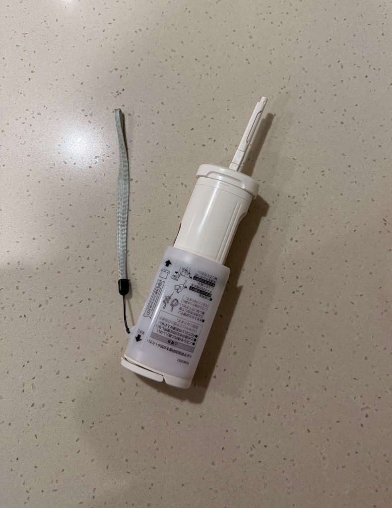 An extended nozzle of a handheld electronic bidet device showing Japanese instruction labels on the body.
