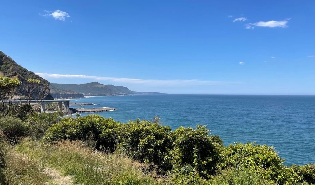 The Sea Cliff Bridge over the ocean next to green coastal cliffs on a sunny day.