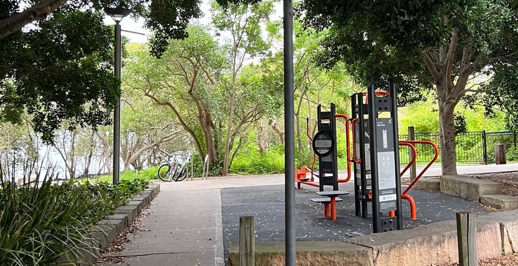 Outdoor park exercise equipment installed on a rubber safety surface next to a concrete walkway.